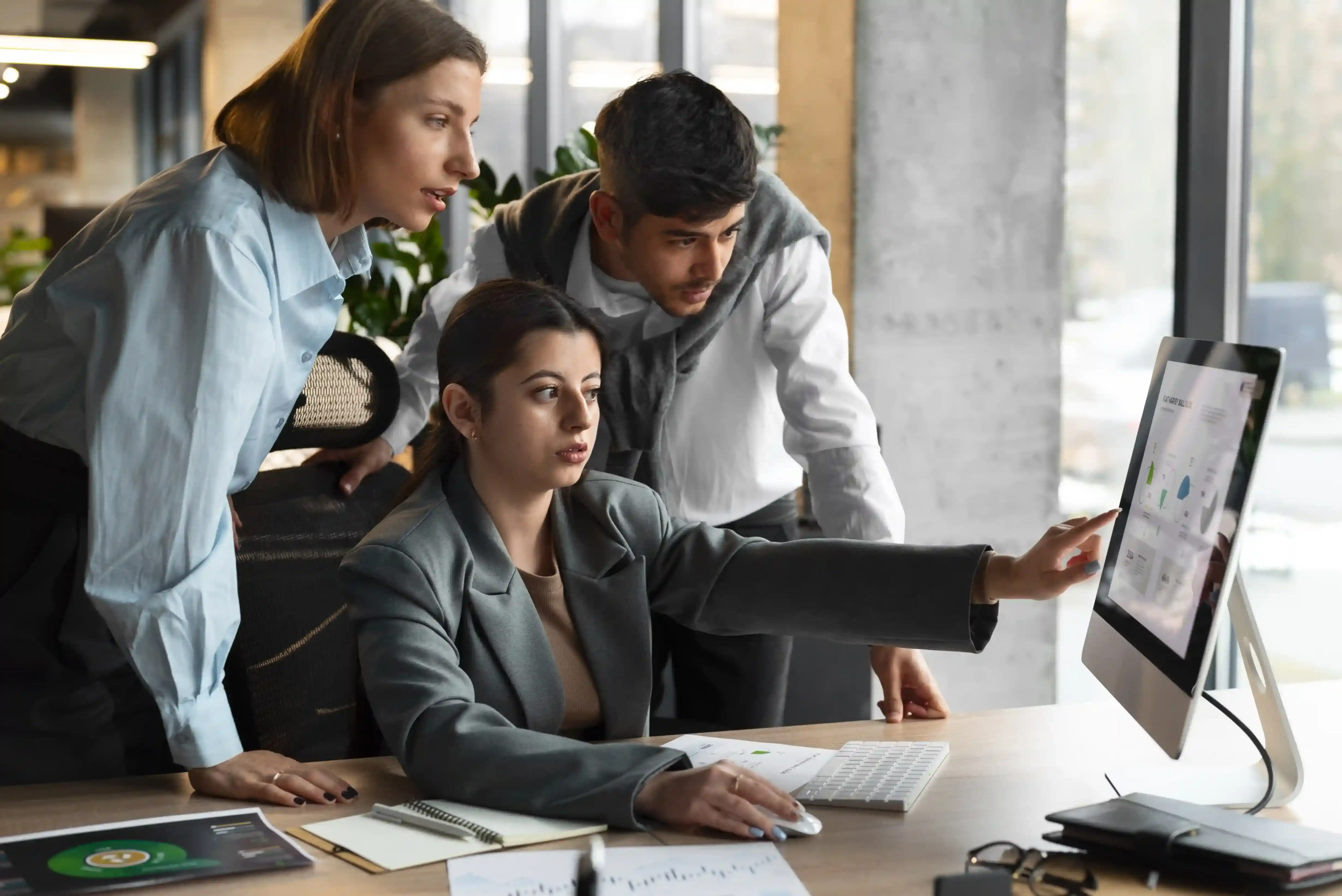 A creative operations manager reviewing project progress on a monitor with two colleagues