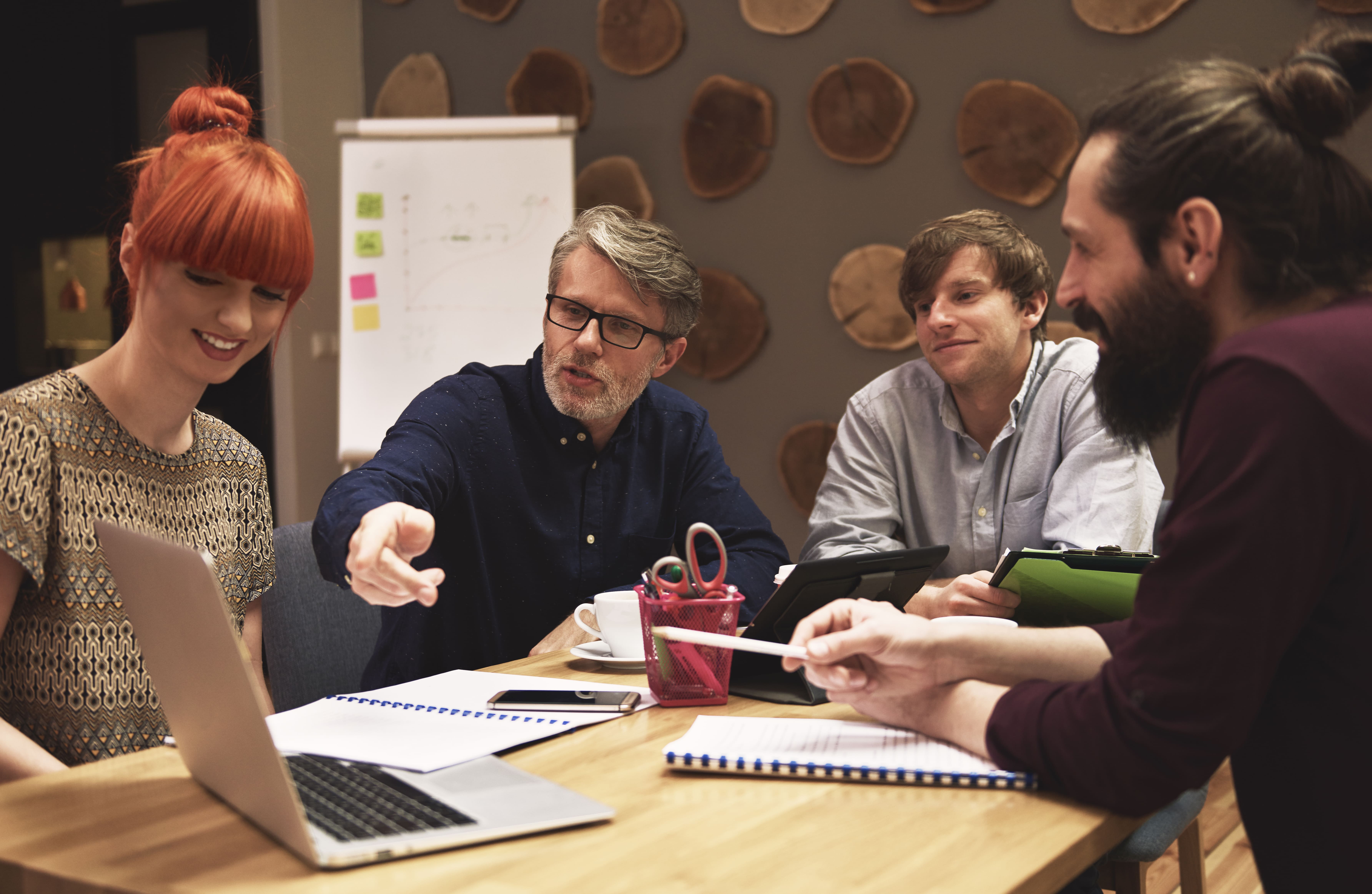 Content writers discussing a brief around a meeting table with laptops and notebooks